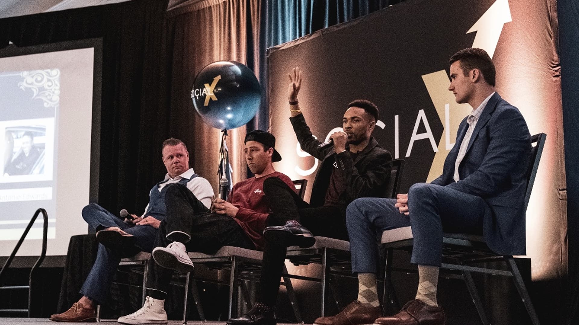 Antonio Edwards speaking with his hand raised during a panel on the Social X stage